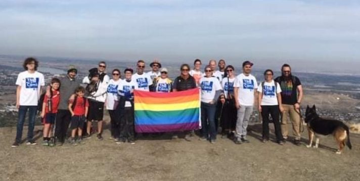 Folx at the top of Badger Mountain holding a Pride Flag. The sky is blue with white wisps of clouds.